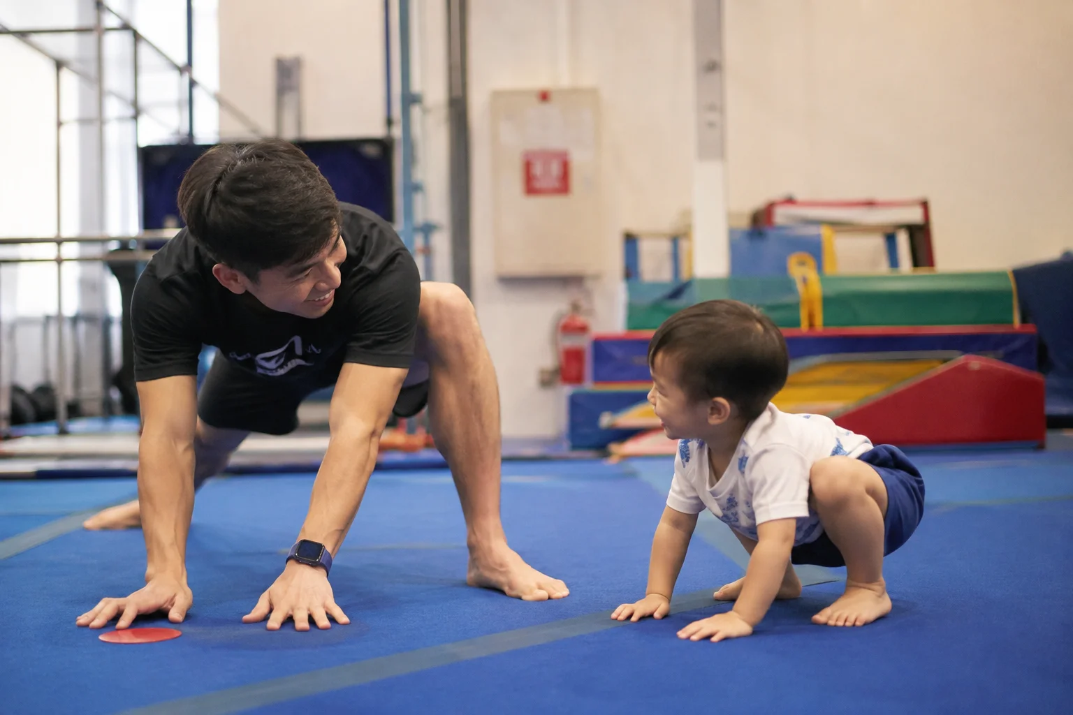 Dad and toddler doing floor gymnastics together on blue mat at Flykidz, Petaling Jaya